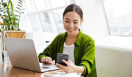 Girl at laptop looking at her smartphone